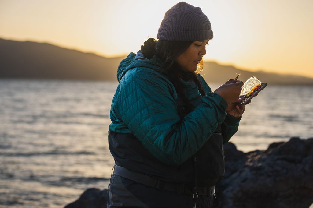 Woman selecting a fly from box while flyfishing at sunset.