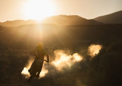 Silhouette of motocross rider on dirt trail in sunset.