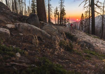 Man in red on gravel tail with red sun setting in background.