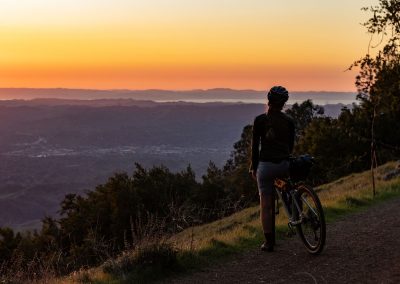 Woman standing on mountain bike looking at beautiful orange and yellow sunset.