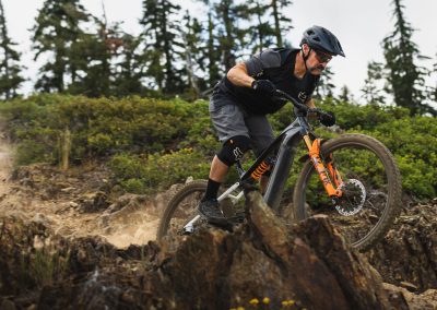 Man with mustache riding e-bike over rough muddy terain.