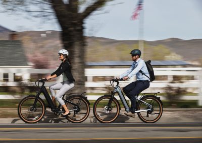 Couple riding e-bikes with helmets and blurred background with American flag.