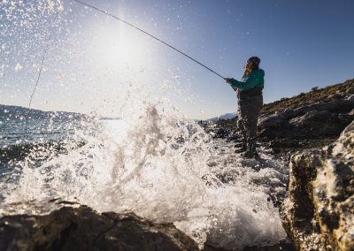 Woman standing on bank of lake fly fishing with water splashing in lens.