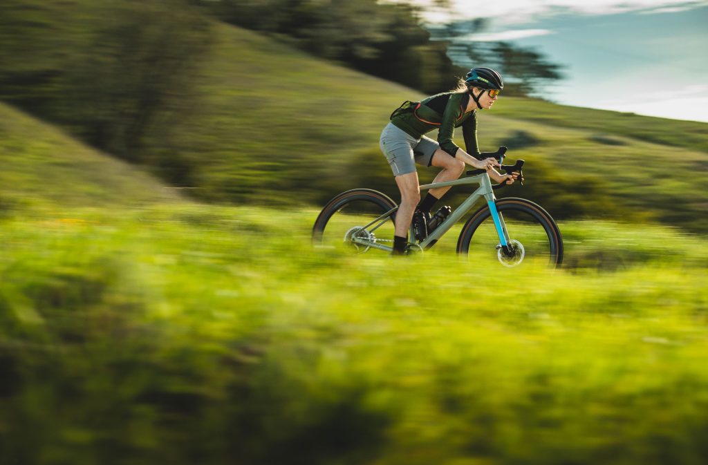 Woman riding gravel bike going fast in green meadow. Photo by Ryan Cleek
