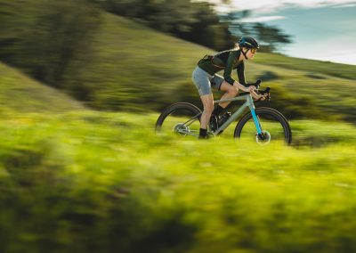 Woman riding gravel bike going fast in green meadow.