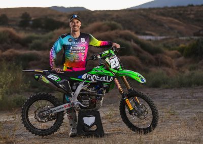 Man with race gear on standing in front of motocross bike.