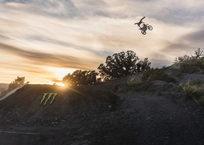 Huge superman air off motocross bike with sun setting and monster energy logo.