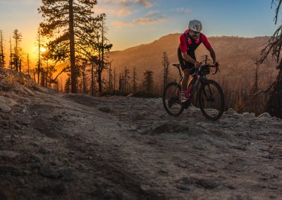 Man riding on gravel trail with orange sunset in background.