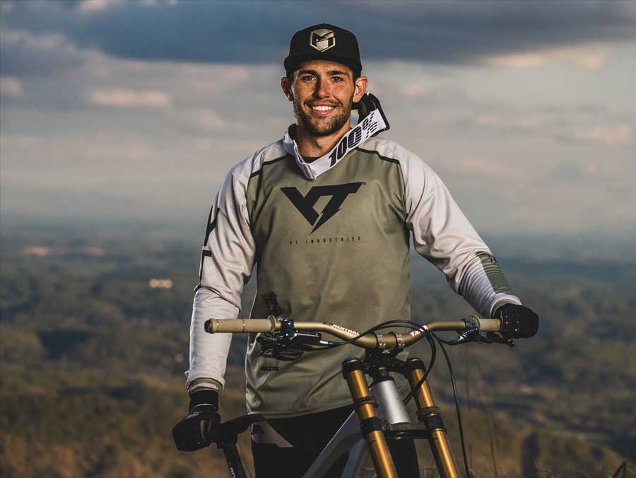 Rider standing in front of bike with sponsored gear on. 