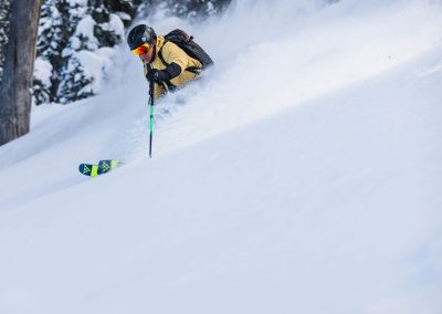 Close up of man skiing in open powder with snow flurries pillowing up behind him.