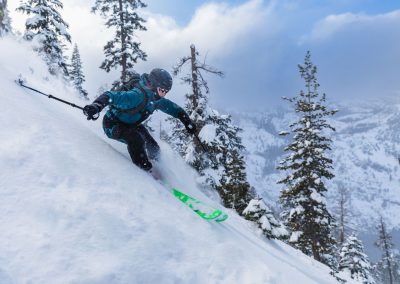 Woman skiing in powder down steep slope in backcountry.