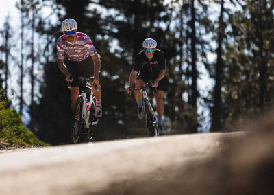 two road cyclists just reaching crest of hill wearing colorful eyewear.