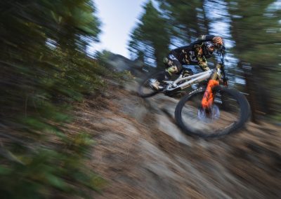 Mountain biker charging down steep trail with blurred forest in background.