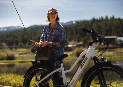 woman standing by e-bike with fly fishing gear.