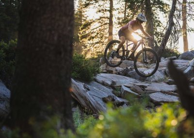 Woman mountain biker riding over rocks and boulders in forest.